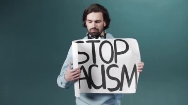 Mavi kazaklı çekici sakallı bir adam ırkçılığa karşı bir poster gösteriyor. 
