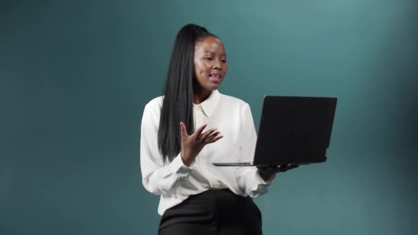 Bej kapüşonlu güzel bir Afrikalı kız bilgisayarını arkadaşlarıyla sohbet etmek, gülümsemek ve el kol hareketi yapmak için kullanıyor. — Stok video