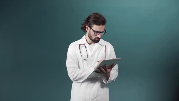 Um jovem médico de vestido branco está escrevendo algo em um tablet guardando em suas mãos — Vídeo de Stock