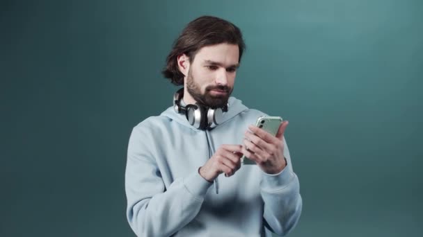 Ένας όμορφος γενειοφόρος με μπλε πουλόβερ χρησιμοποιεί τηλέφωνο και ψάχνει στο ίντερνετ. — Αρχείο Βίντεο