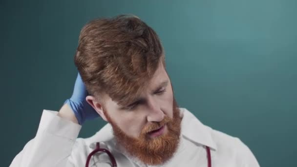 Um jovem médico de casaco branco com um estetoscópio ao redor do pescoço sente uma forte dor de cabeça — Vídeo de Stock
