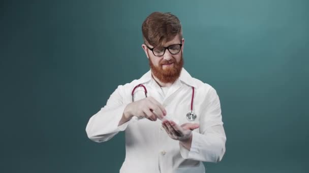 Мужчина в белом медицинском платье и очках дезинфицирует руки и смотрит в камеру. — стоковое видео