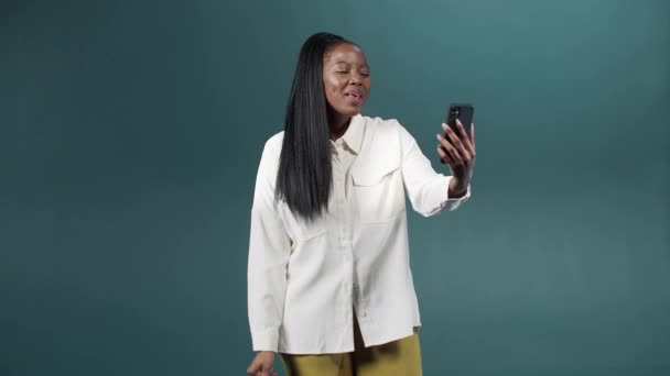 Une fille africaine dans un chemisier classique blanc parle sur l'appel vidéo avec son ami et agitant les bras — Video