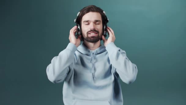 Een aantrekkelijke jongeman in een blauwe trui luistert naar muziek en knikt met zijn hoofd — Stockvideo