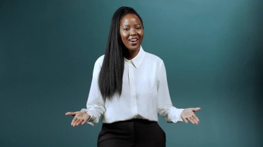 Çekici, uzun saçlı Afrikalı bir kız kameraya konuşuyor, gülümsüyor ve el kol hareketi yapıyor.