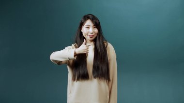 Neşeli Asyalı bir kadın baş parmağını kaldırıyor ve gülümsüyor.