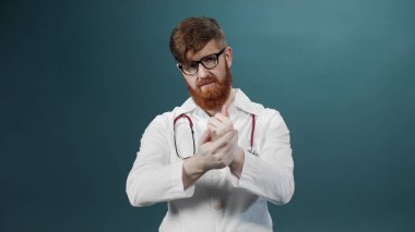 Beyaz elbiseli ve gözlüklü bir adam ellerini sterilize ediyor ve kameraya bakıyor.