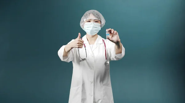 Beyaz üniformalı çekici bir Asyalı genç doktor kameraya bakıyor ve Coronavirus 'a karşı aşısı olan bir ampul gösteriyor. — Stok fotoğraf