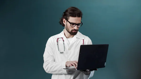 An adult doctor in a medical uniform is using his laptop for searching though the Internet — Stock Photo, Image