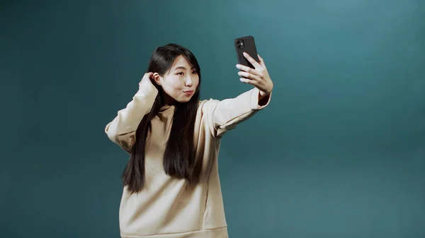 Chica bonita con el pelo largo y oscuro en sudadera con capucha beige hace selfie en su nuevo teléfono —  Fotos de Stock