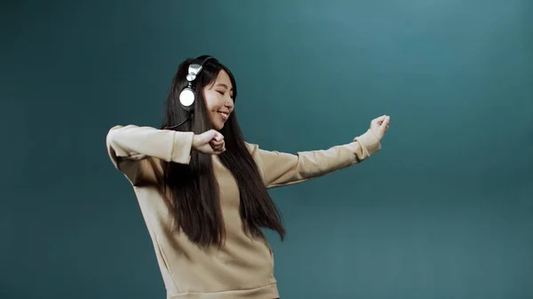 Joven mujer deportiva china con sudadera beige mostrar movimientos de baile con auriculares en —  Fotos de Stock