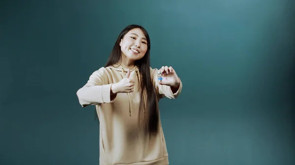 Een leuke jonge Aziatische dame houdt een ampul vaccin tegen het coronavirus en toont een duim omhoog — Stockfoto