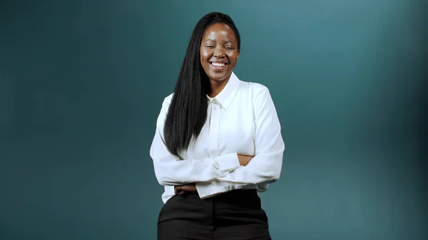 A dark skin woman dressed in white shirt and black pants is standing, smiling and looking at the camera Stock Photo