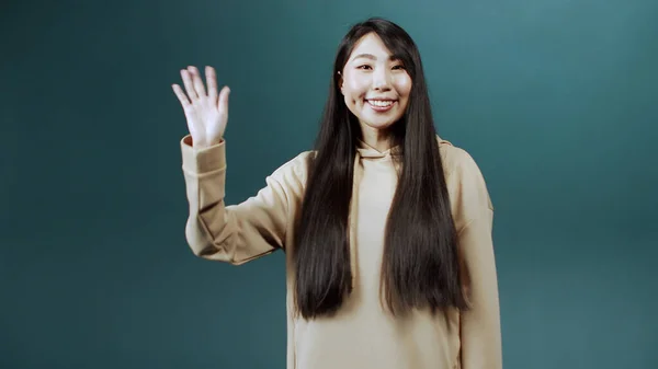 Attraente allegra ragazza cinese con i capelli lunghi in posa per la fotocamera, sorridendo e agitando le mani Foto Stock Royalty Free