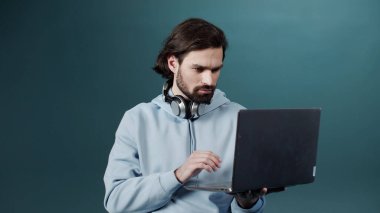 Güzel, beyaz tenli sakallı bir adam elinde bir dizüstü bilgisayar tutuyor ve internette arama yapıyor.