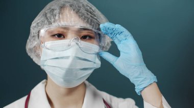 Tıp üniformalı yorgun bir kadın gözlüğünü tamir ediyor ve kameraya bakıyor.