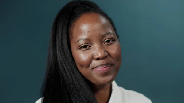 Siyah kadın, uzun saçlı, yeşil stüdyo arka planında poz veren, gülümseyen.