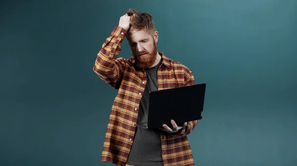 En ung kille med rött hår och skägg avslöjar seriös attityd hålla en bärbar dator — Stockfoto