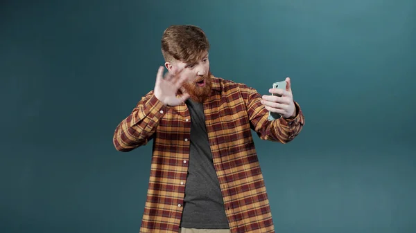Энтузиастичный молодой рыжий мужчина делает видеозвонок с помощью камеры возле зеленой стены — стоковое фото