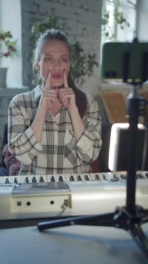 Bir kadın tripodun üzerinde telefonun önünde oturuyor. Sentezleyiciyi çalıyor ve şarkı söylüyor. Dudaklarını hangi pozisyonda daha iyi şarkı söyleyeceğini gösteriyor. Yüksek kaliteli FullHD görüntüler