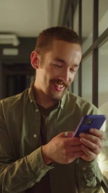 Genç bir erkek öğrenci pencerenin yanında duruyor, uzaklara bakıyor ve sonra internette gülümseyen yazılar okuyor. Yüksek kaliteli FullHD görüntüler