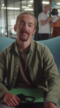 Genç beyaz bir adam üniversitede sandalyede oturuyor, gülümsüyor ve kameraya bakıyor. Yüksek kaliteli FullHD görüntüler