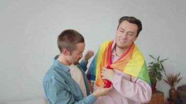 İki yakışıklı genç adam lgbt bayrağı gösteriyor, gülümsüyor ve sarılıyorlar. Yüksek kaliteli FullHD görüntüler