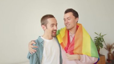 Igbt bayrağıyla kaplanmış iki genç adam yan yana duruyor ve birbirleriyle gülümsüyorlar. Yüksek kaliteli FullHD görüntüler