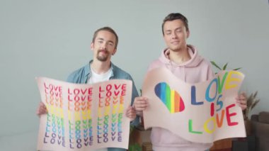 İki yakışıklı genç adam Igbt posterlerini astı, birbirlerine baktılar ve gülümsediler. Yüksek kaliteli FullHD görüntüler