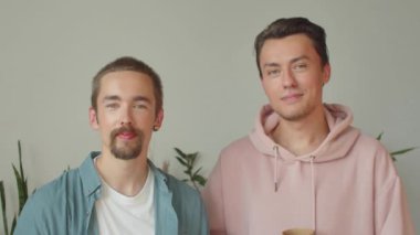 Pembe kapüşonlu yakışıklı bir adam en iyi arkadaşının yanında duruyor, kameraya bakıyor, gülümsüyor ve içeceğini içiyor. Yüksek kaliteli FullHD görüntüler