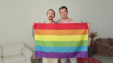 İki çekici genç adam yan yana kameraya bakıyor ve elinde bir lgbt bayrağı tutuyor. Yüksek kaliteli FullHD görüntüler