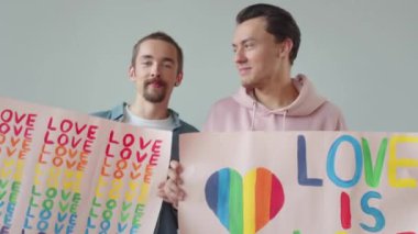 İki genç adam Igbt posterleri gösteriyor, birbirlerine bakıp gülümsüyorlar. Yüksek kaliteli FullHD görüntüler