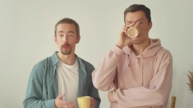 Pembe kapüşonlu yakışıklı genç bir adam, erkek arkadaşı kamerayla konuşurken bir içecek içiyor ve el kol hareketi yapıyor. Yüksek kalite 4k görüntü