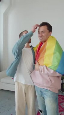 İki genç adam birlikte duruyor, üzerlerinde lgbt bayrağı var, ve bir tanesi en iyi arkadaşının saç stilini düzeltiyor. Yüksek kaliteli FullHD görüntüler