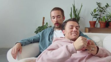 Tatlı bir Igbt çifti oturma odasındaki kanepede oturuyor, konuşuyor ve el ele tutuşuyorlar. Yüksek kaliteli FullHD görüntüler