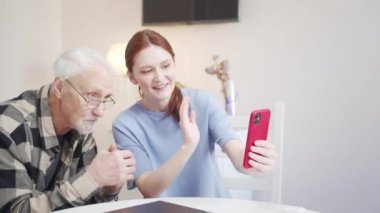 Kadın ve o, gözlüklü gri saçlı bir baba, video iletişimi yoluyla akrabalarıyla iletişim kurmak için telefonu kullanıyor. Müfettişi selamlar ve ellerini sallarlar.