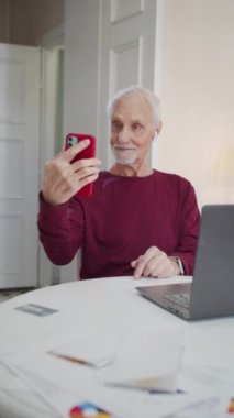 Yaşlı adam rahat bir dairede telefonla fotoğraf çekiyor. Kameraya poz veren yaşlı vatandaş, gülümsüyor ve şaşırıyor. Yüksek kaliteli FullHD görüntüler