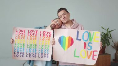 İki yakışıklı genç adam Igbt posterleri gösteriyor, birbirlerine bakıp gülümsüyorlar. Yüksek kaliteli FullHD görüntüler