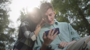 Hoş bir çift telefonda bir şey izliyor, konuşuyor ve gülümsüyor, birlikte parktalar. Yüksek kaliteli FullHD görüntüler