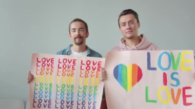 İki yakışıklı genç adam Igbt posterleri gösteriyor, birbirlerine bakıp gülümsüyorlar. Yüksek kaliteli FullHD görüntüler