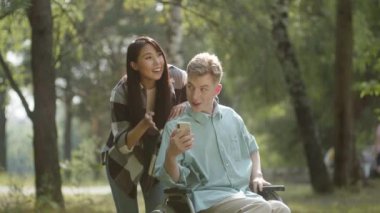 Halka açık bir parkta, güzel bir havada, genç bir çift arkadaşlarıyla FaceTime 'da konuşuyor, gülümsüyor ve sohbetin tadını çıkarıyor, ağır çekimde. Yüksek kalite 4k görüntü