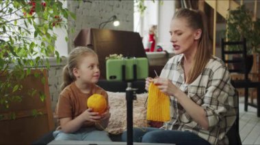 Anne ve kızı akıllı telefon kullanarak canlı yayın yapıyorlar. Ellerinde yün yumakları ve örgü iğneleri tutuyorlar ve izleyicilerle iletişim kuruyorlar. Yüksek kalite 4k görüntü