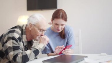 Kızı, gözlüklü yaşlı babanın modern telefon kullanmayı öğrenmesine yardım ediyor. Yüksek kalite 4k görüntü