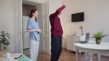 Bir kadın bir emeklinin egzersiz yapmasına yardım eder. Bir adam elleriyle egzersiz yapar ve bilgisayarda egzersiz seyreder. Yüksek kalite 4k görüntü