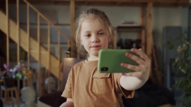 Çocuk elinde bir akıllı telefon tutuyor ve ön kamerada kendi resimlerini çekiyor. Kız gülümsüyor. Yüksek kalite 4k görüntü