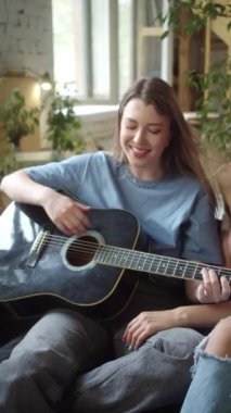 İki kız kanepede astarlı odada oturup gitar çalıyor ve ağır çekimde şarkılar söylüyor. Yüksek kaliteli FullHD görüntüler