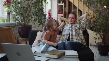 Geniş bir çatı katında koltukta rahatça oturan bir kadın. Çocuğu elini tutuyor ve ev ödevinde yardım istiyor. Bir kadın yorgun bir şekilde iç çeker ve egzersizleri defterden inceler. Yüksek kalite 4k görüntü