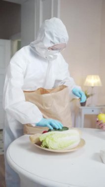 Koruyucu giysili bir kadın yaşlı bir kadına yardım eder. Sosyal bir program için bir paket meyve ve sebze getirdi. Yüksek kaliteli FullHD görüntüler