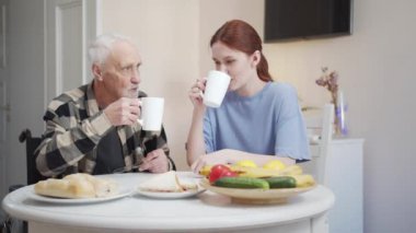 Büyükbaba ve kadın masada oturup çay içiyorlar. Kadehleri tokuşturup gülümserler. Yüksek kalite 4k görüntü