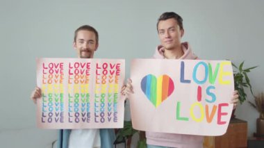 İki genç yakışıklı, Igbt posterlerini indirip birbirlerine bakıp gülümsüyorlar. Yüksek kaliteli FullHD görüntüler